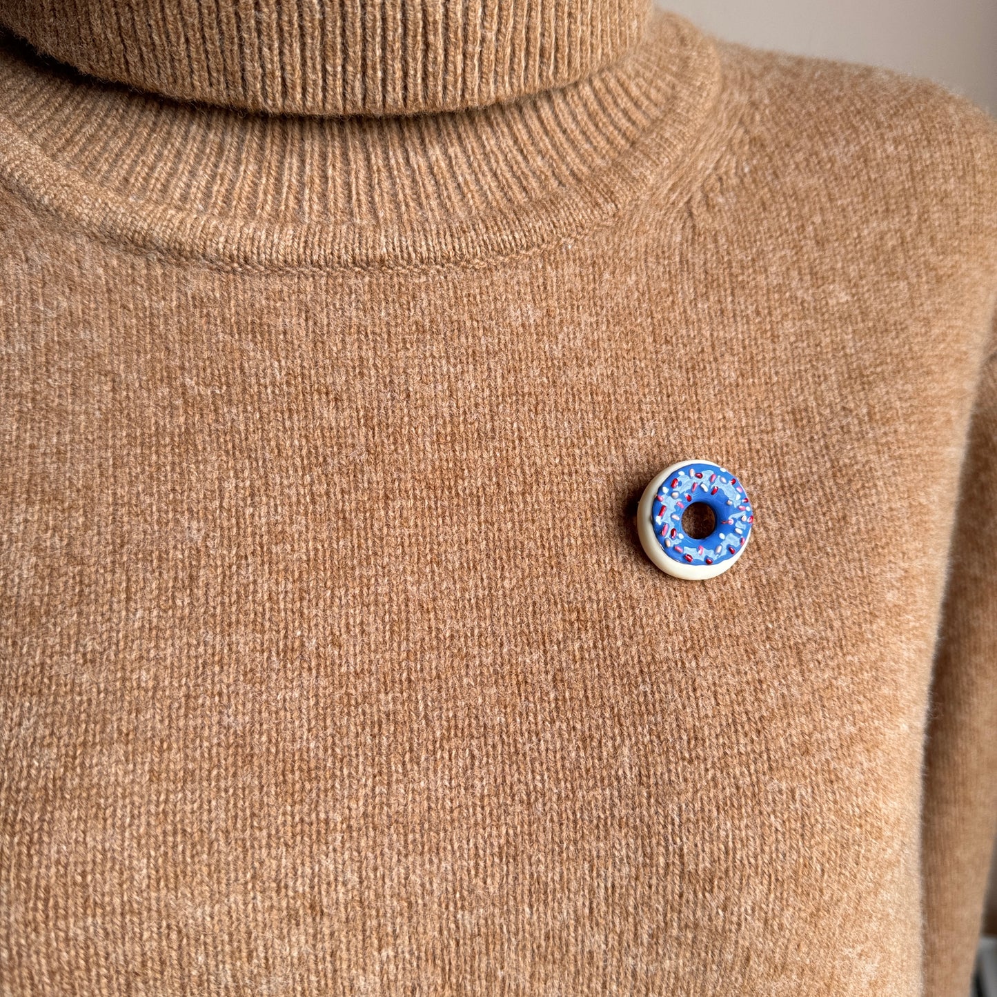 Playful donut-shaped brooch with glaze and sprinkles worn on sweater