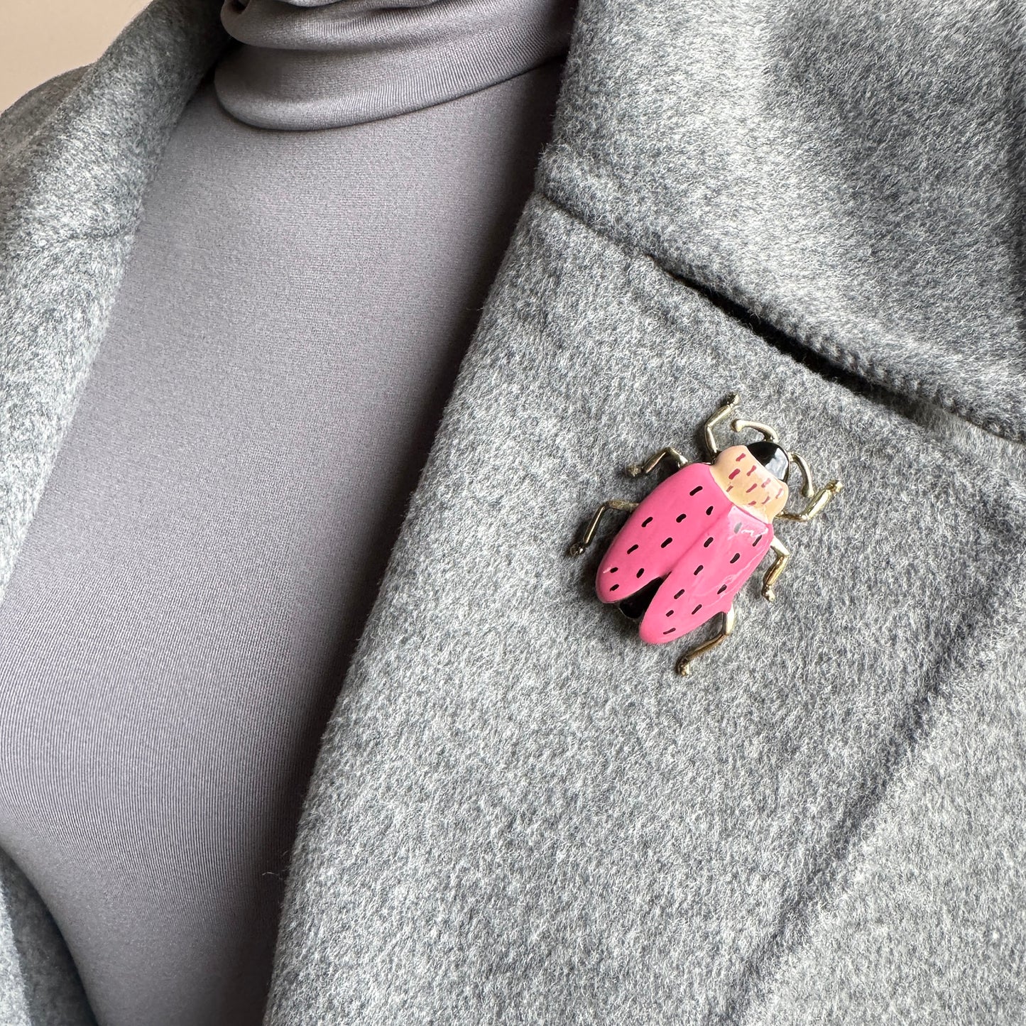 Retro-style beetle brooch in pink and gold worn on a gray coat