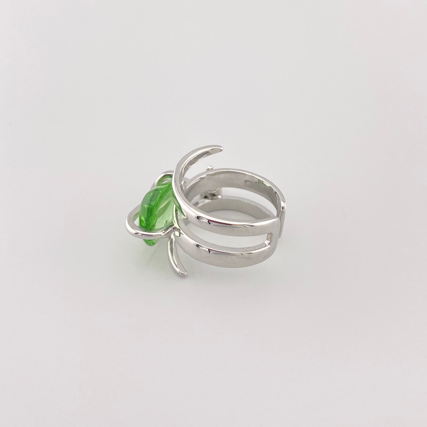 Green crystal ring with silver band placed on a tree branch for contrast