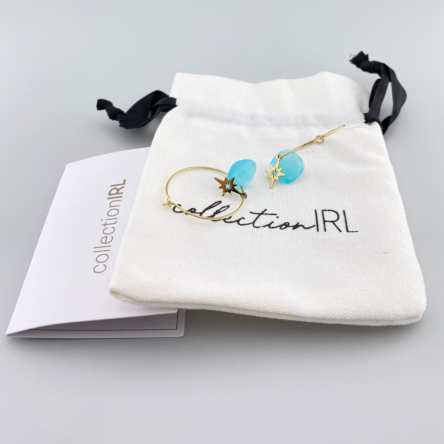 Boucles d’oreilles IRL dorées avec pierre bleue et pendentif étoile présentées dans l’écrin de la marque