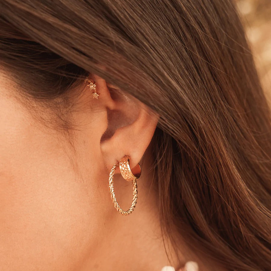 Twisted gold hoop earrings catching light on the ear