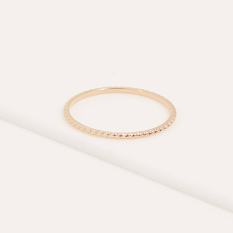 Anillo minimalista IRL chapado en oro con detalle trenzado sobre superficie clara