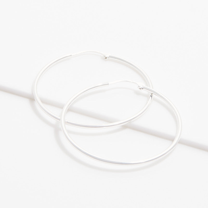 Boucles d’oreilles créoles IRL argentées présentées à plat sur fond clair
