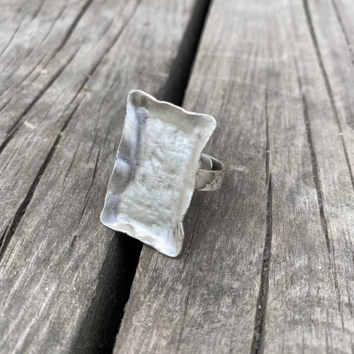 Anillo plateado rectangular con pátina sobre fondo rústico de madera