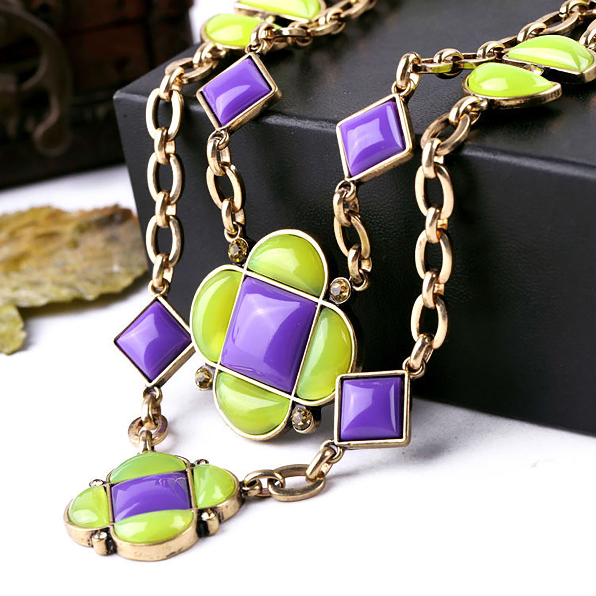 Necklace with geometric shapes in purple and lime green on a gold chain.