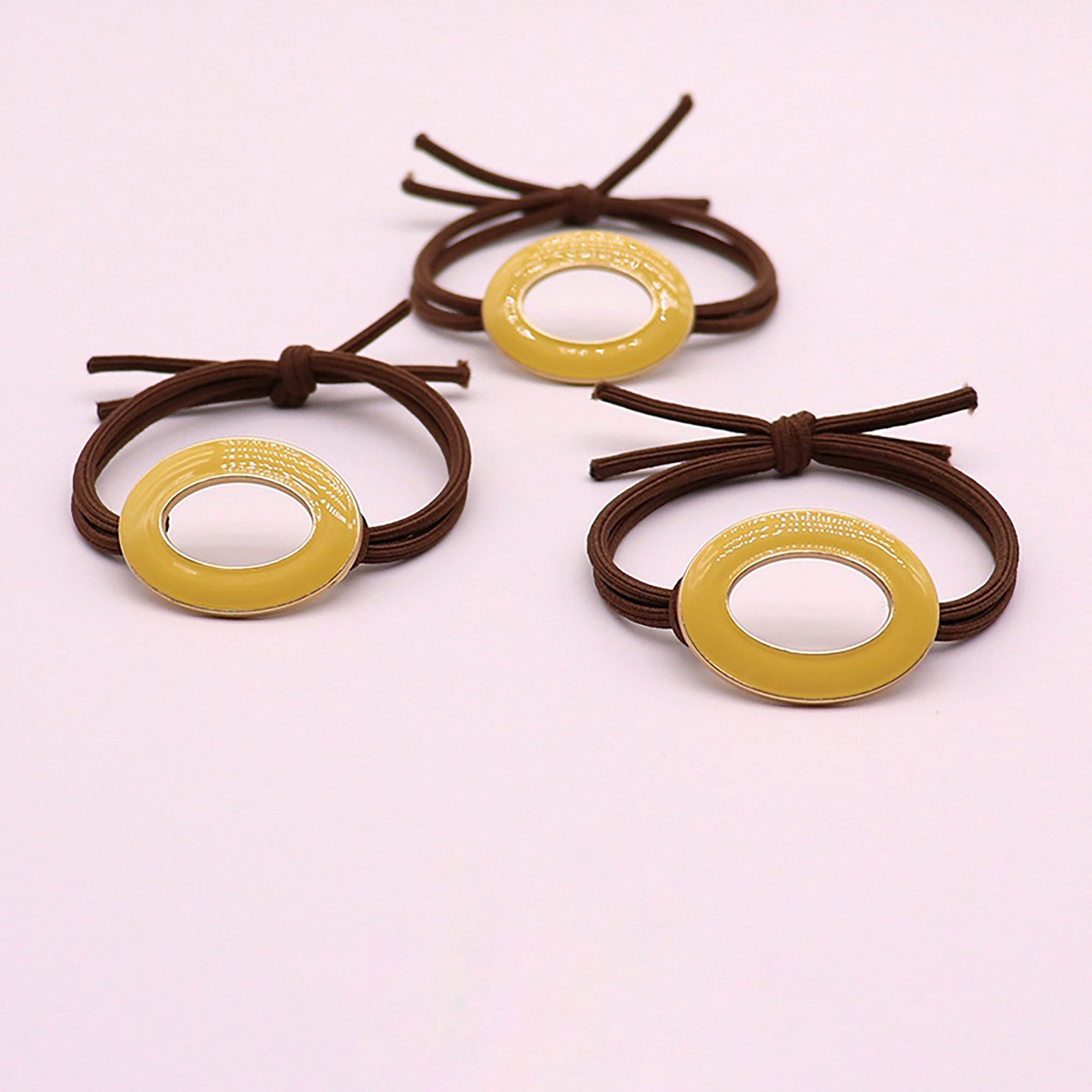 Hair tie in brown with an oval charm coated in yellow enamel.