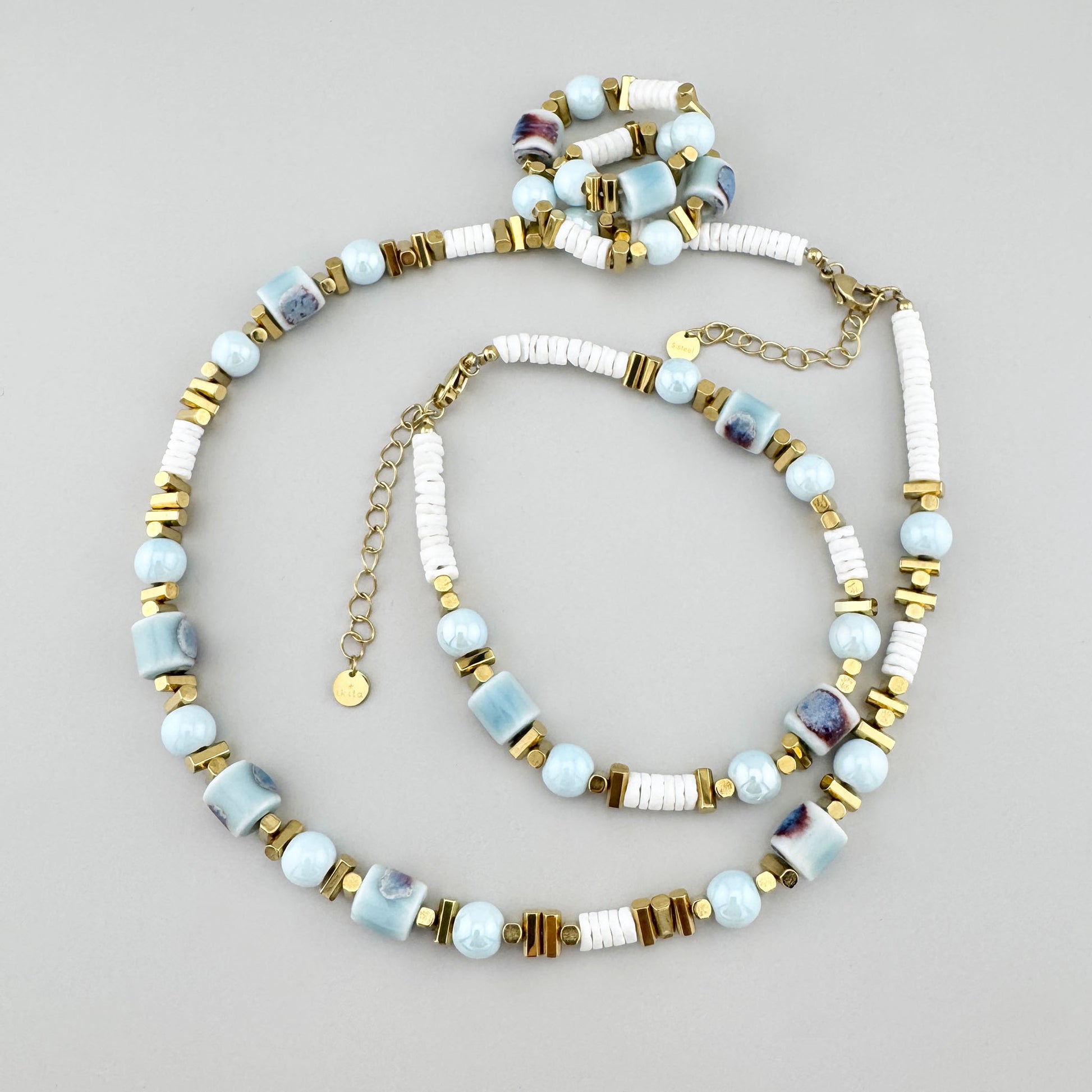 Collar con cuentas cerámicas azules, discos blancos y separadores dorados, marca francesa Ikita.