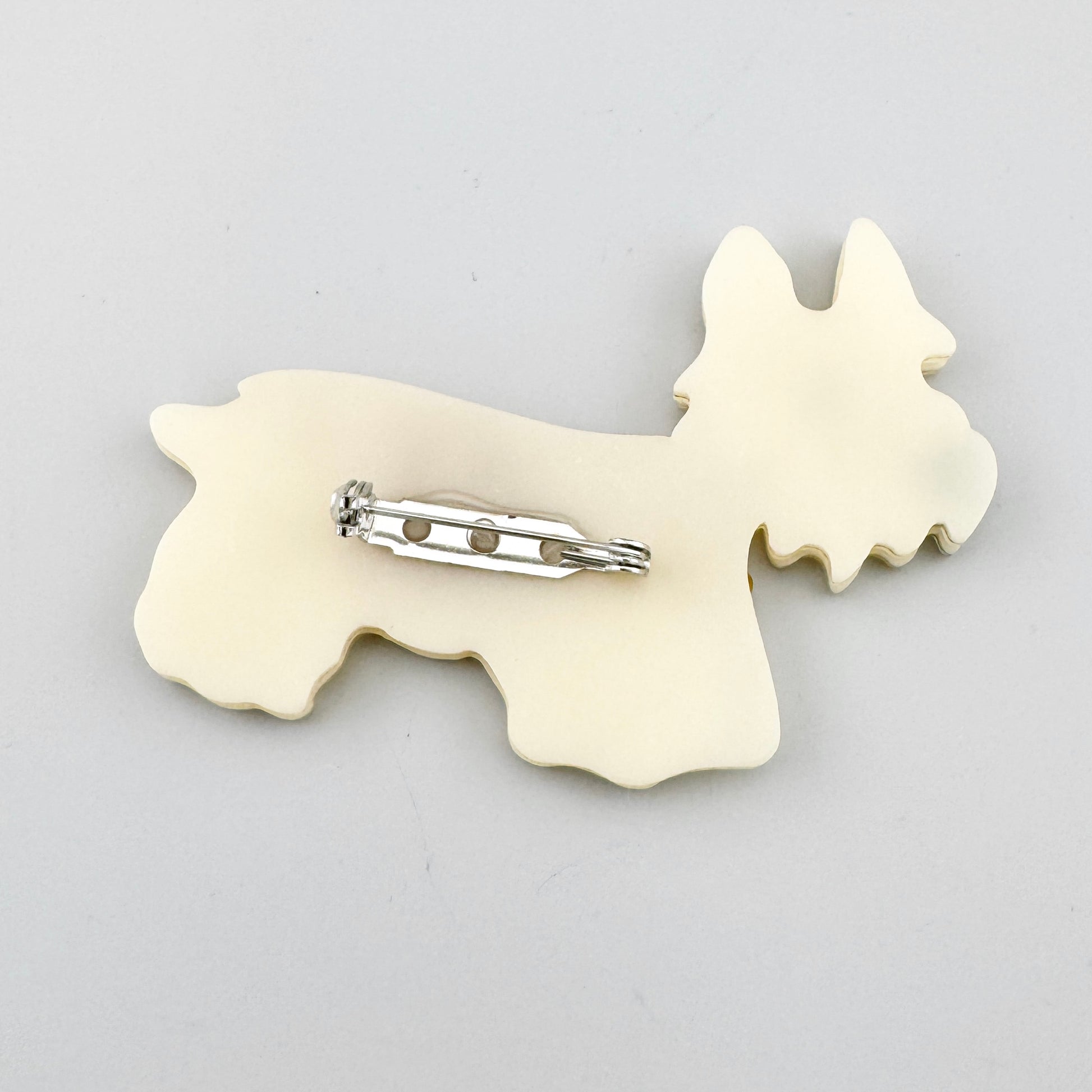 Broche con forma de perro en acrílico perlado y abrigo amarillo con textura craquelada, de la marca española Sonata.