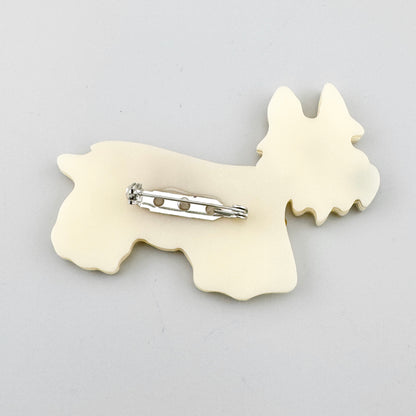 Broche con forma de perro en acrílico perlado y abrigo amarillo con textura craquelada, de la marca española Sonata.