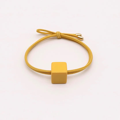 Yellow hair tie with a minimalist square-shaped ornament.