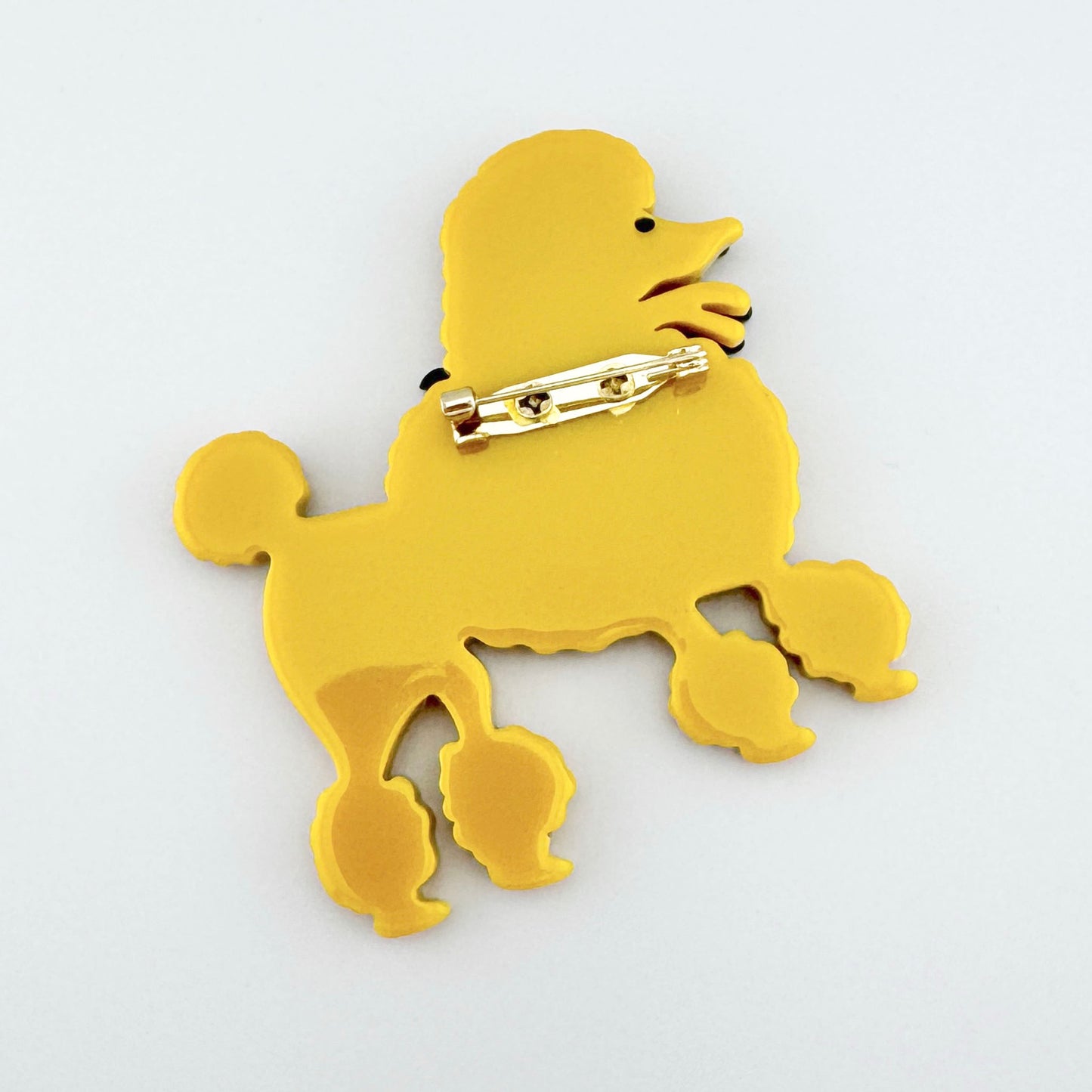 Broche en forma de caniche amarillo con lazo negro, hecho de material sintético brillante, marca española Sonata.