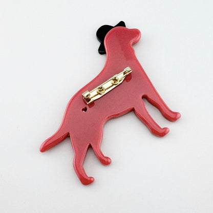 Dog-shaped brooch with a black hat, made of glossy pink coral-tone plastic.