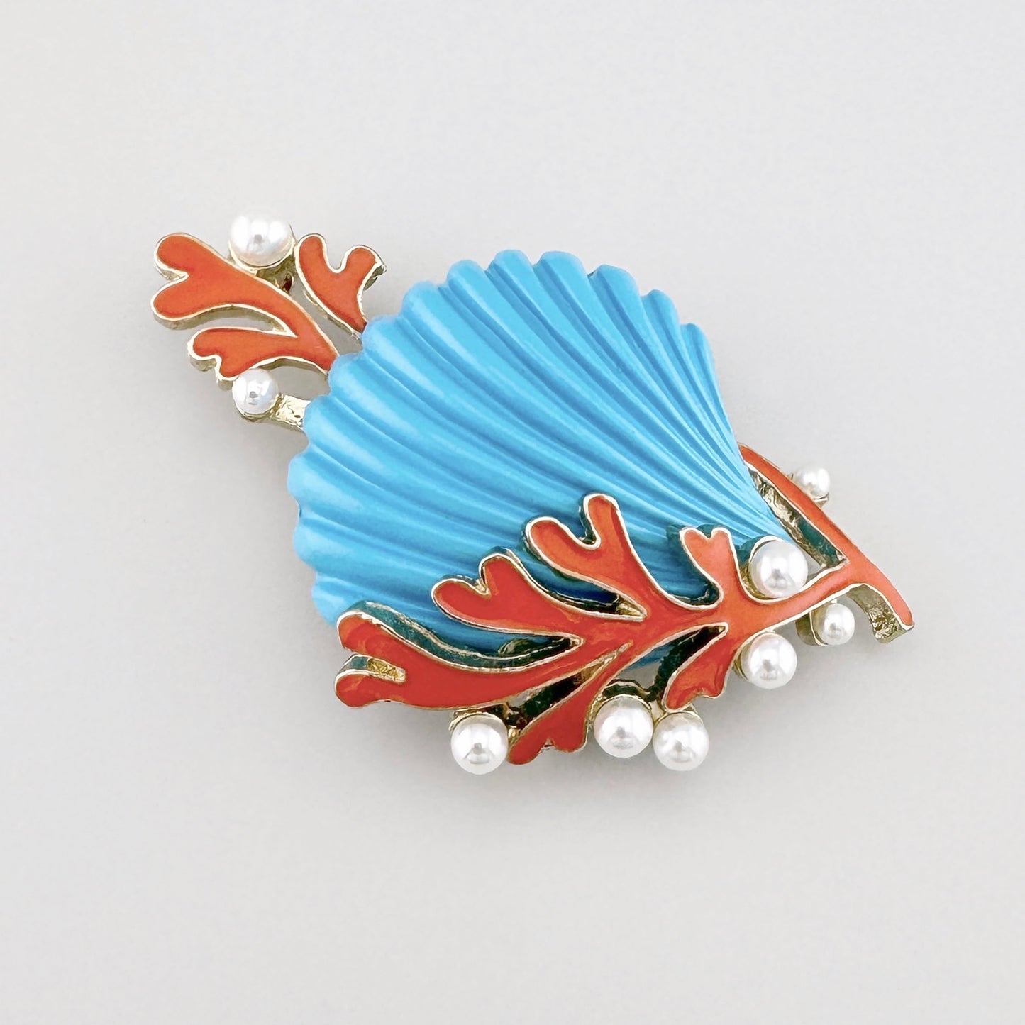 Broche en forma de concha con esmalte azul, decorado con coral y perlas.