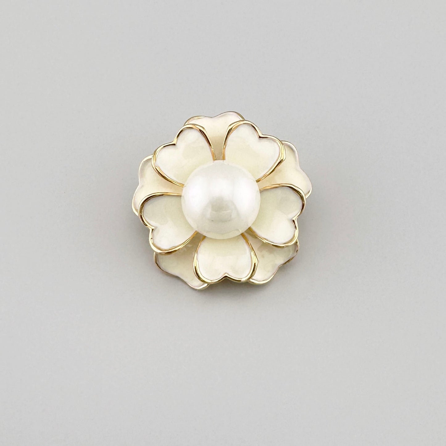 Flower-shaped brooch with a white pearl center and gold accents.