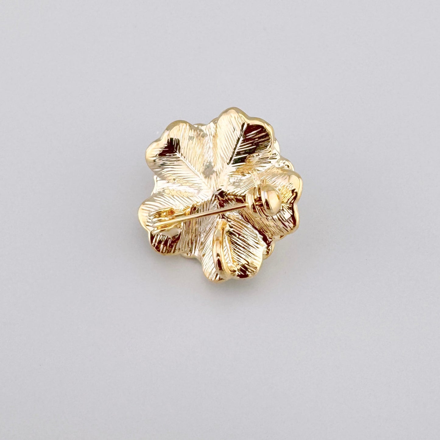 Broche en forme de fleur avec une perle blanche au centre et des accents dorés.