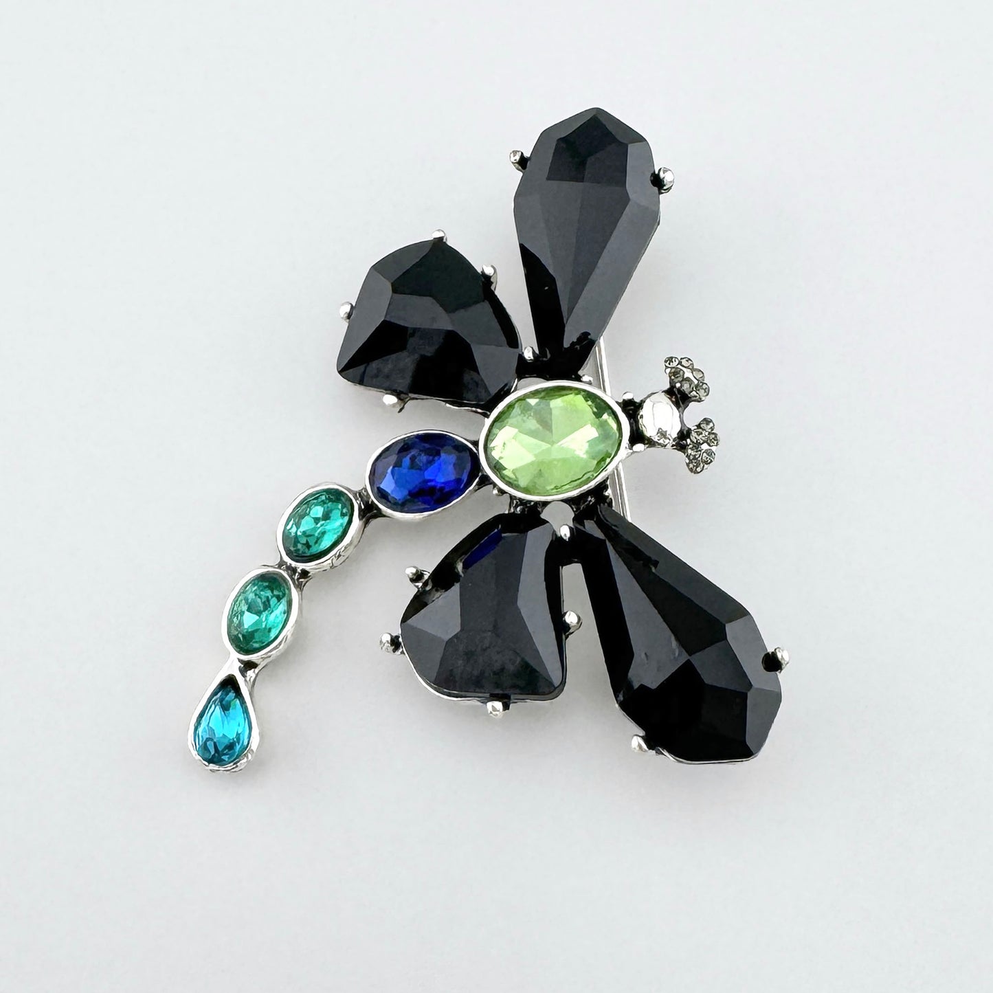 Broche en forma de libélula con alas negras y cristales en tonos verdes, azules y turquesas.