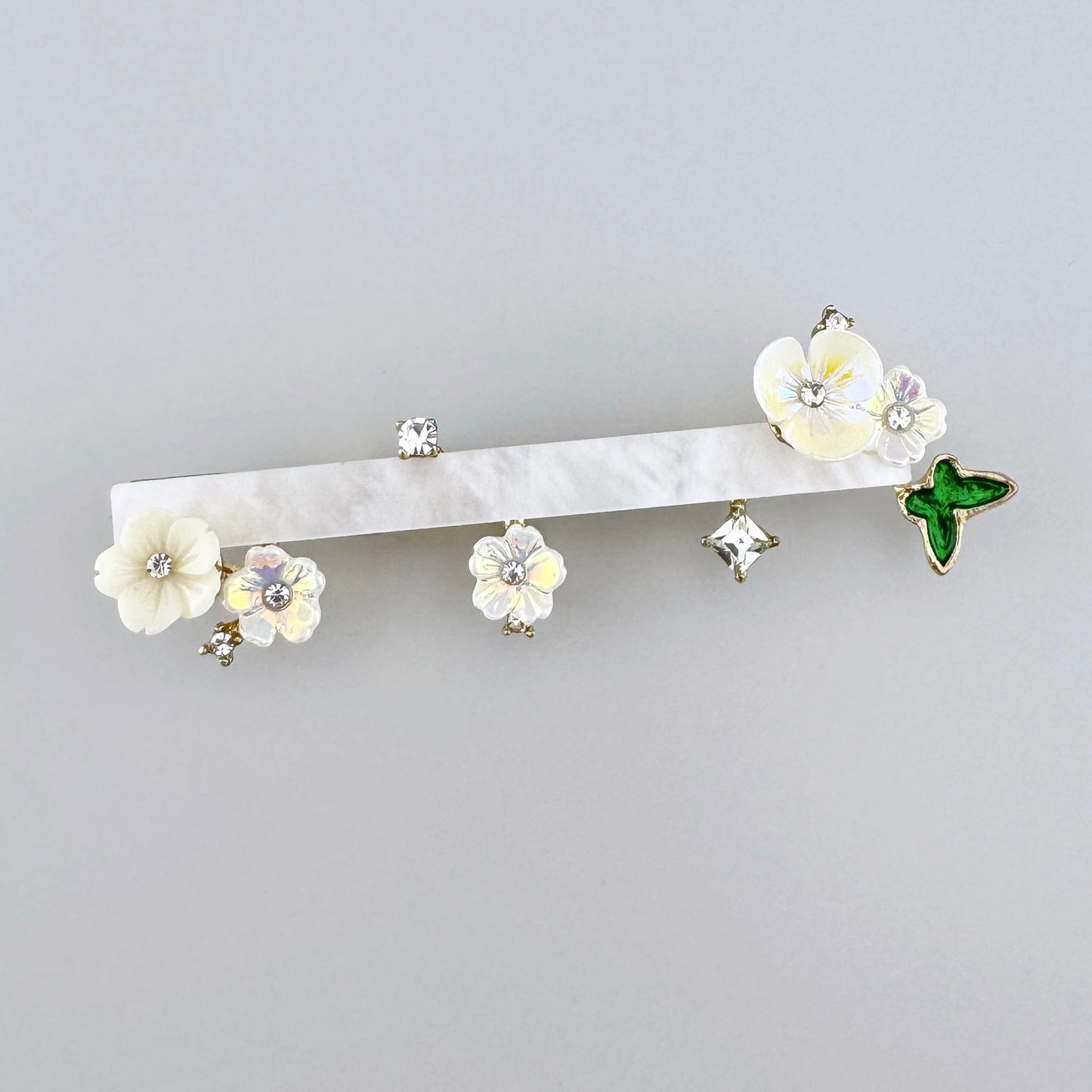 Elegante broche en forma de rama decorado con flores delicadas, cristales y un acento de mariposa verde, marca española Sonata.