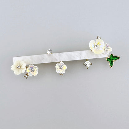 Elegante broche en forma de rama decorado con flores delicadas, cristales y un acento de mariposa verde, marca española Sonata.