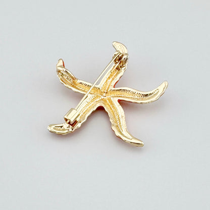 Starfish-shaped brooch, orange with subtle gold accents.