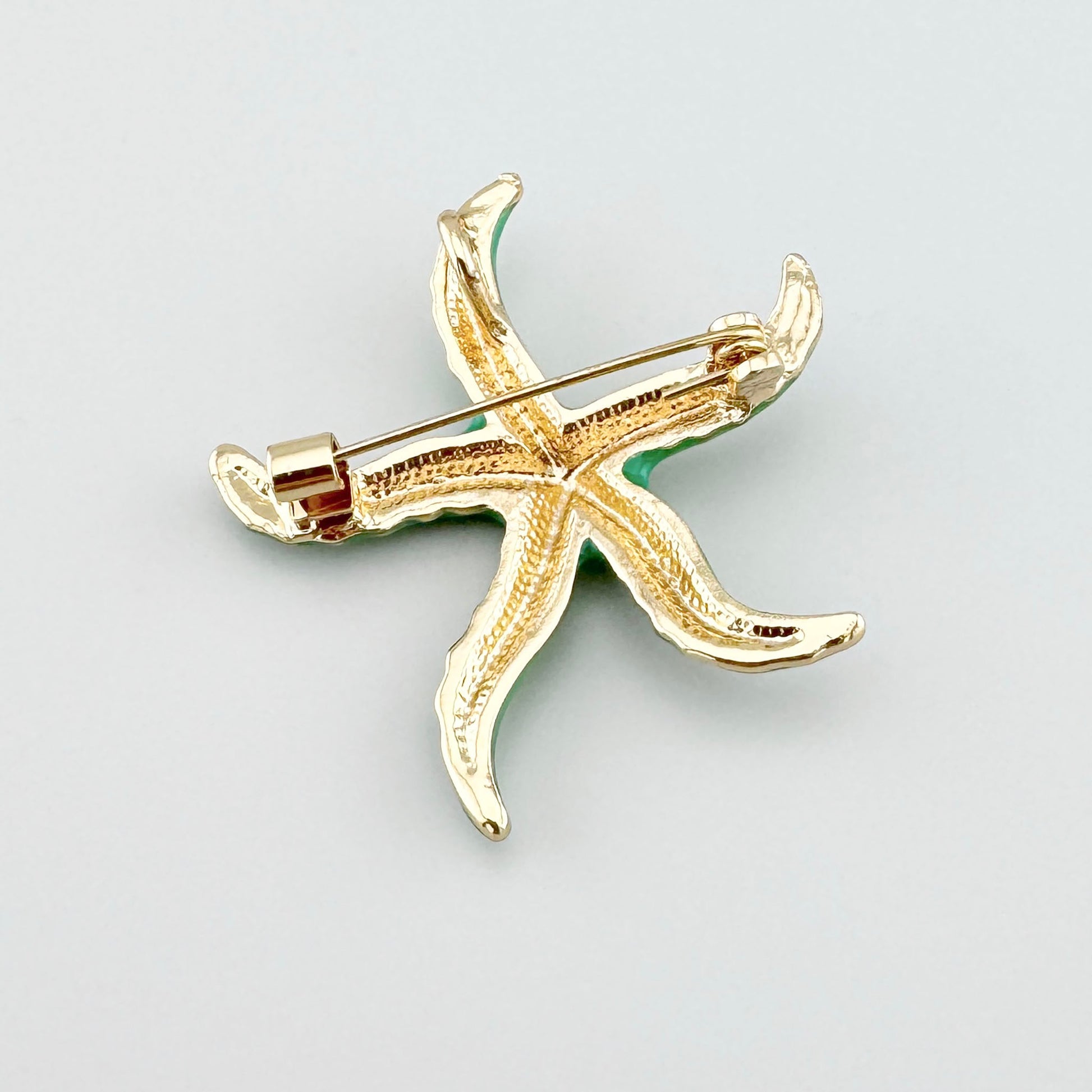 Broche verte en forme d'étoile de mer avec des touches dorées.