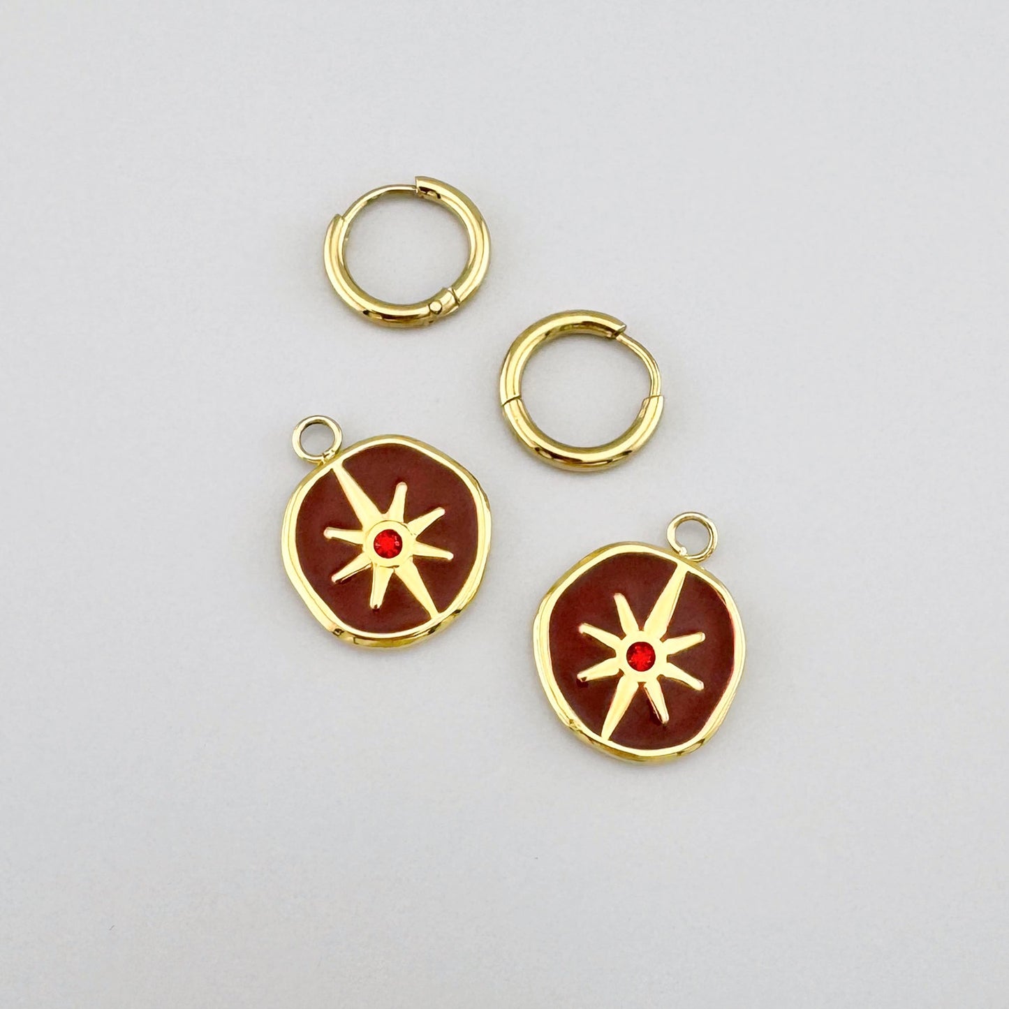 Gold earrings with red enamel, featuring a star motif and a crystal accent.