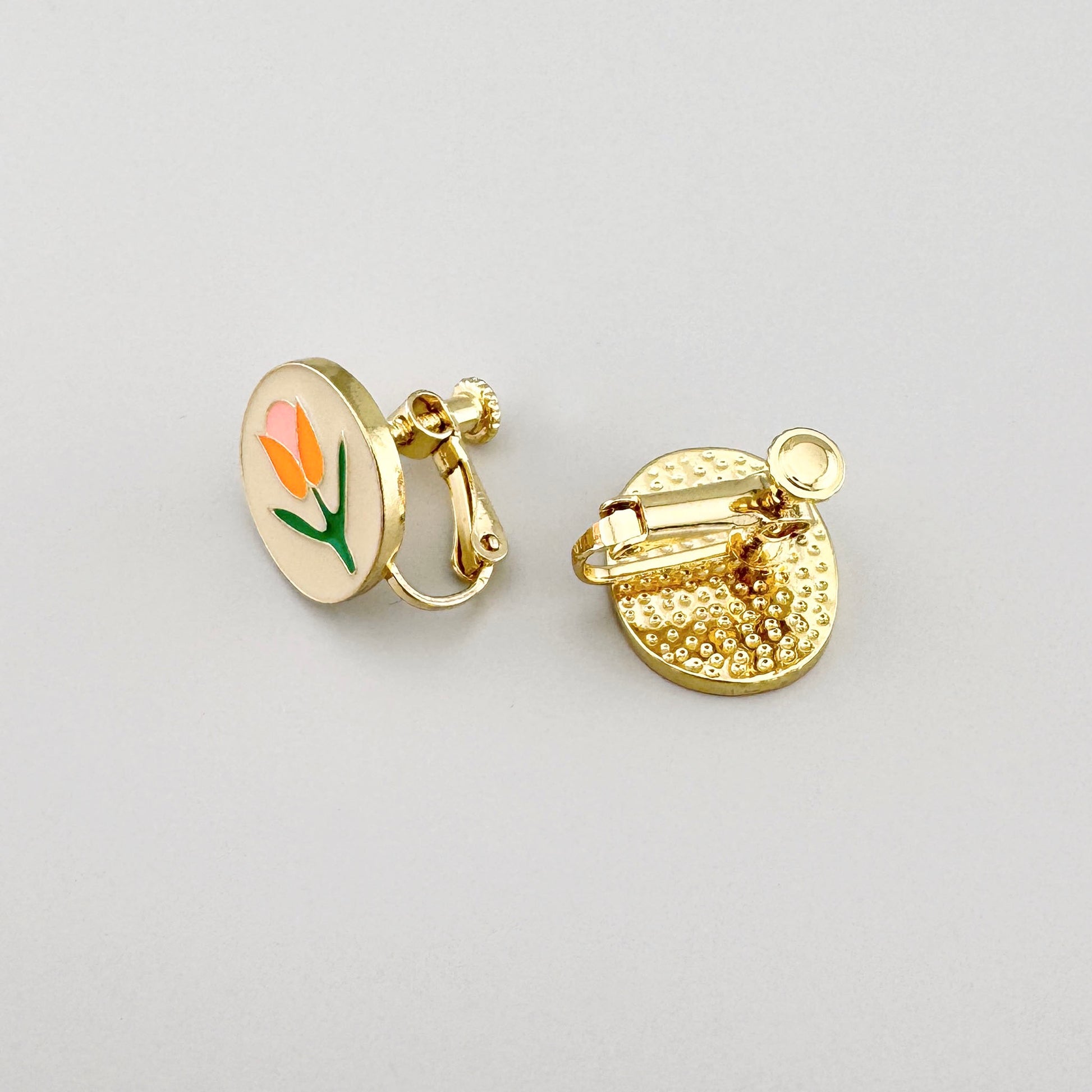 Pendientes de clip con motivo floral en tonos rosa, naranja y verde sobre base dorada.