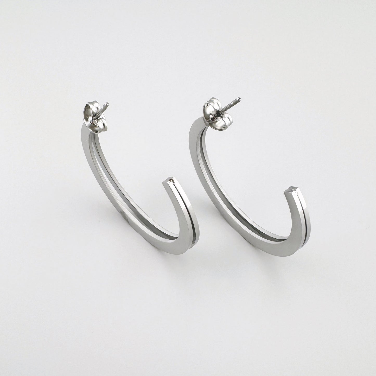 Minimalist earrings with an open half-hoop design in silver color. Brand Maravillas.