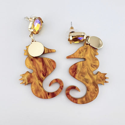 Seahorse-shaped earrings with an amber effect and gold accents.