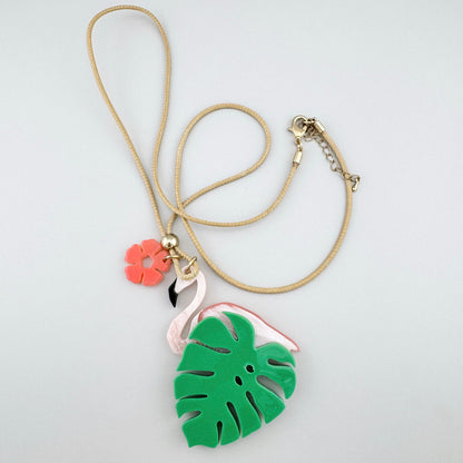 Collier avec pendentif pastel représentant un flamant rose et une feuille de monstera.