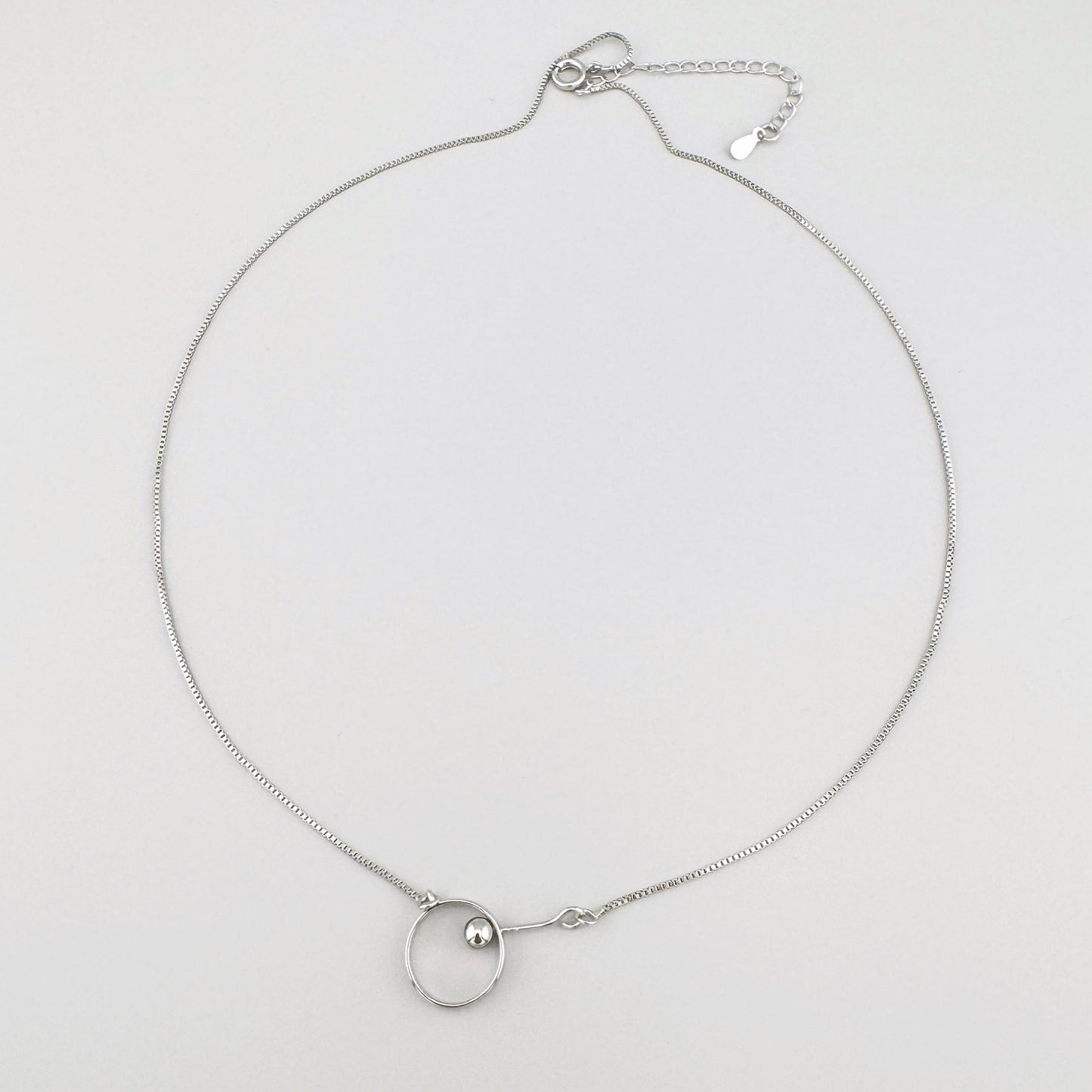 Minimalist necklace with a silver-plated pendant featuring a circle and a small sphere.