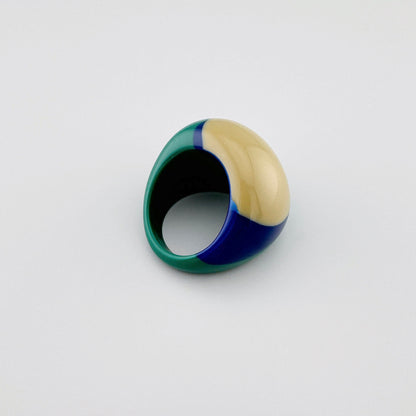 Anillo llamativo en tonos beige, verde y azul marino, hecho de plástico brillante.