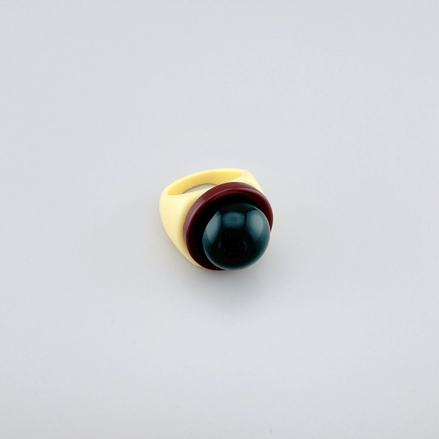 Bague en plastique crème avec sphère verte et accent bordeaux.