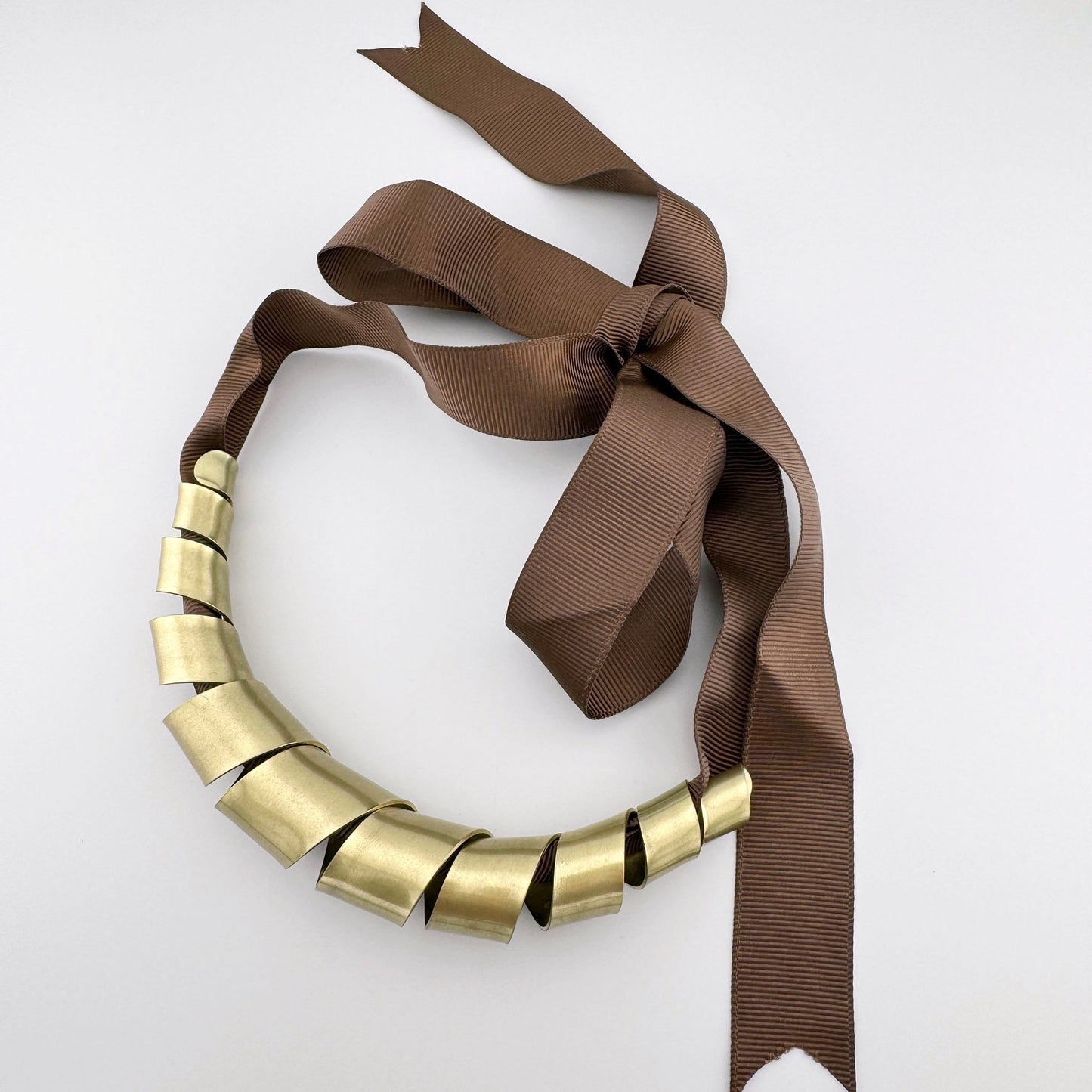 Necklace with spiral-shaped metal elements in antique gold color, tied with a brown ribbon.