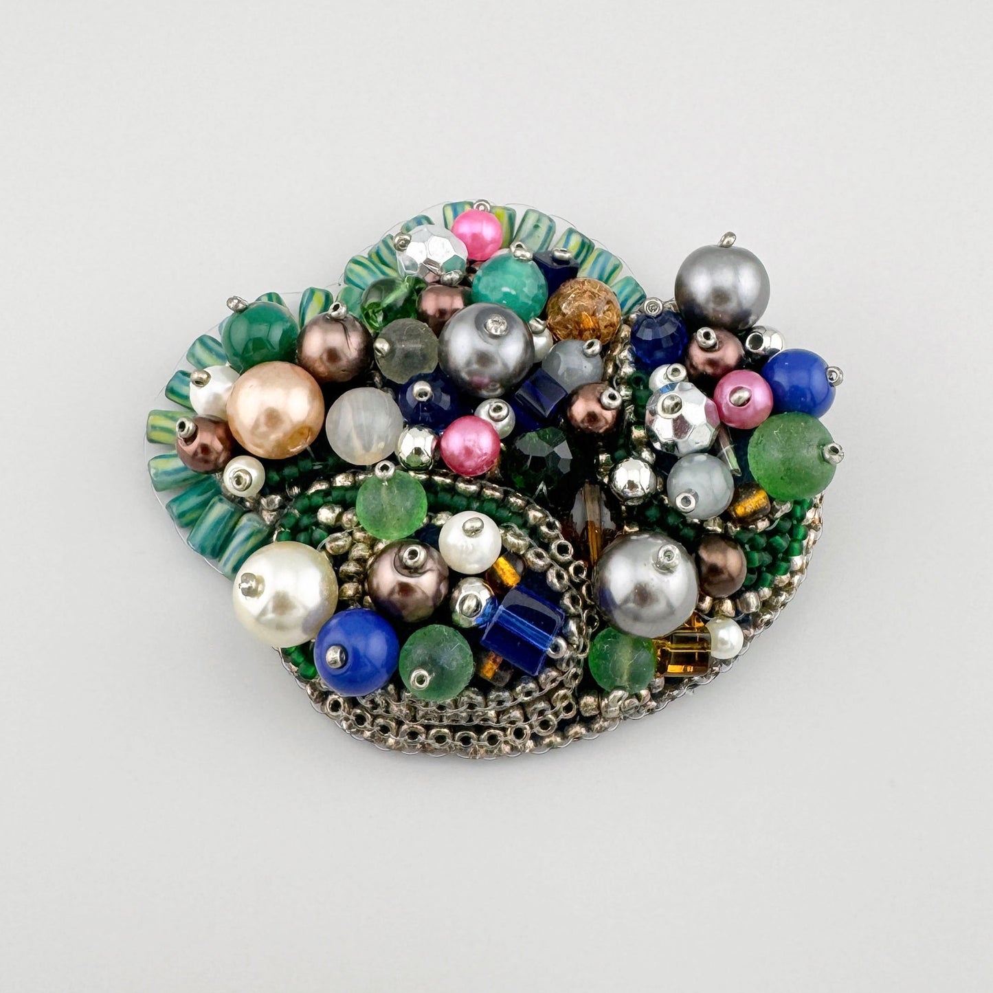 Handmade brooch decorated with beads in shades of green, blue, pink, and pearl.