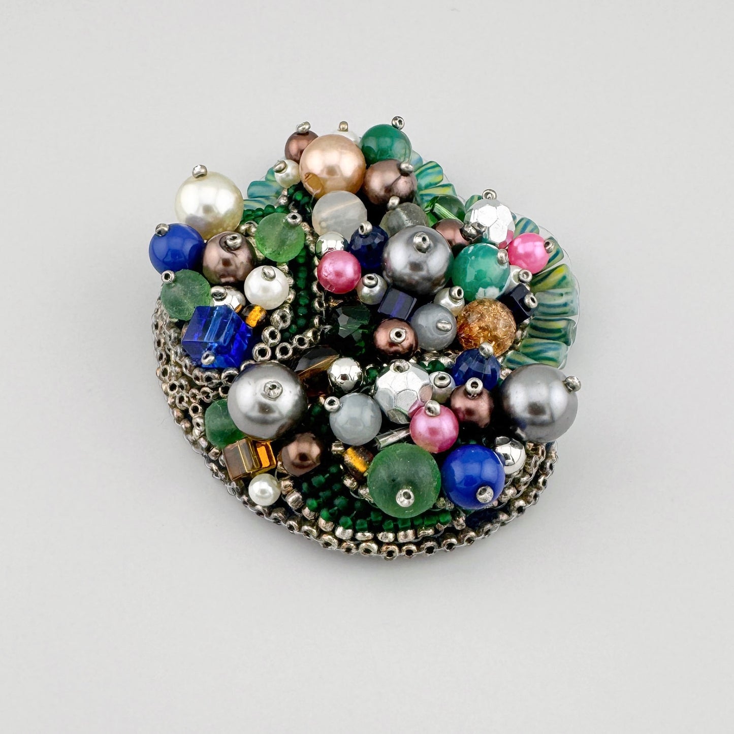 Broche faite à la main, ornée de perles aux teintes vertes, bleues, roses et nacrées.