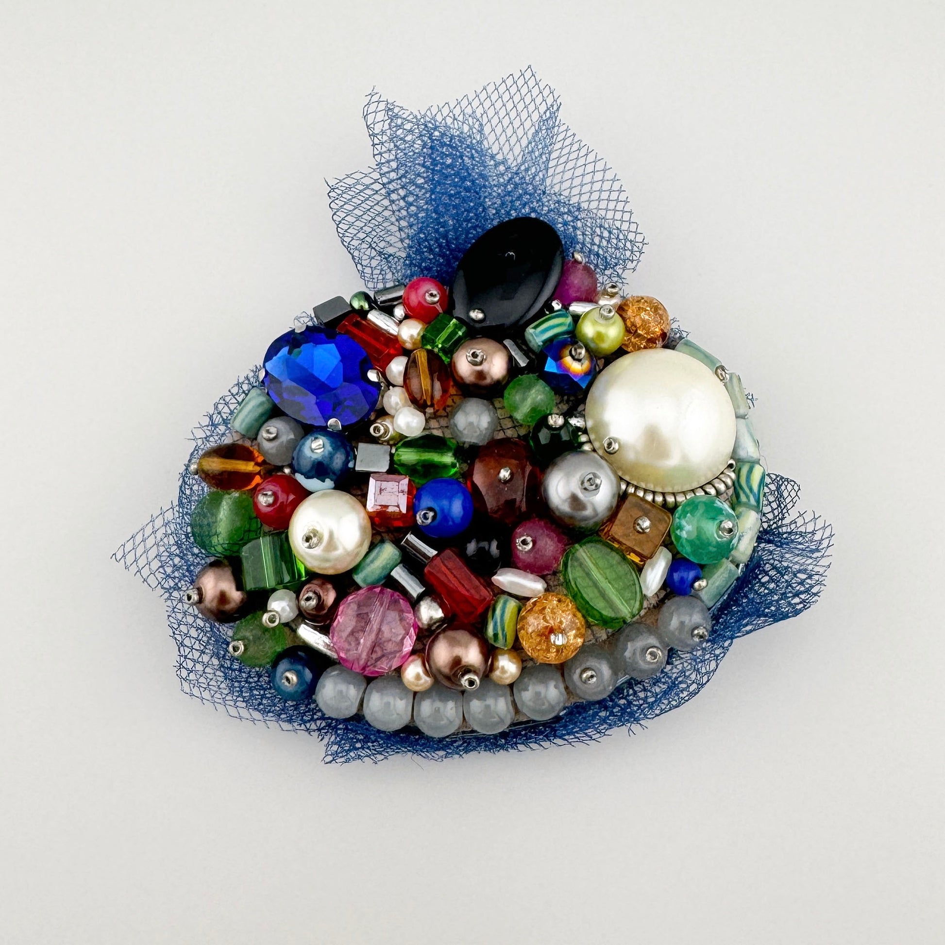 Handcrafted colorful brooch with beads on a navy blue mesh background, Polish brand BroszArt.