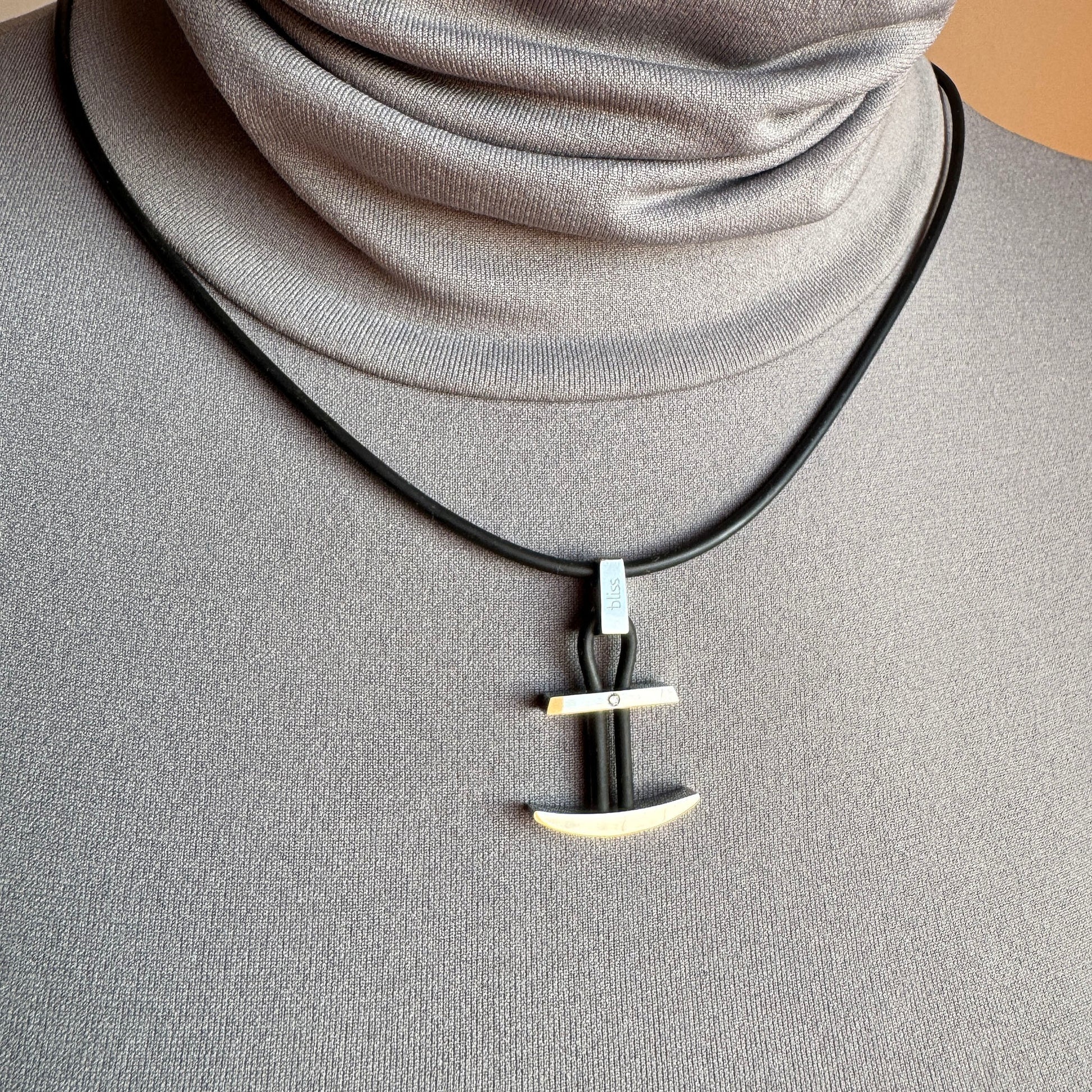Silver anchor pendant on black cord, clean modern line near the collarbone