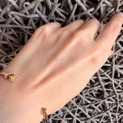 Minimal gold arrow cuff bracelet worn lightly on the wrist with a refined modern feel