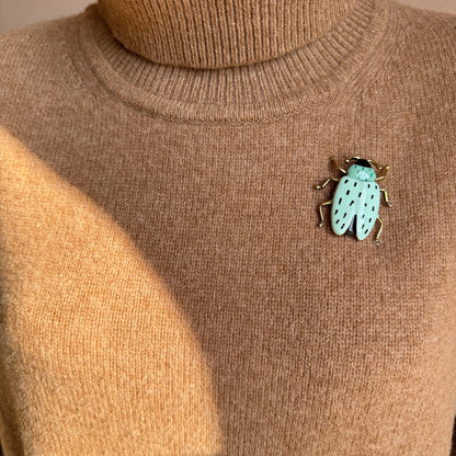 Retro beetle-shaped brooch with turquoise enamel and gold details worn on sweater