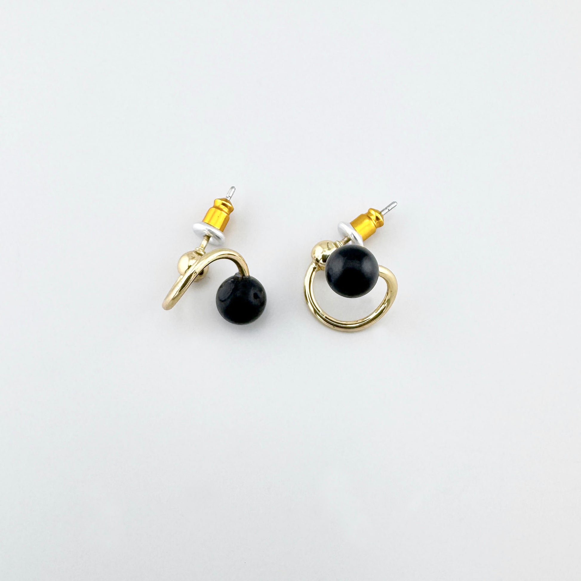Pendientes dorados con piedra negra y silueta en espiral, brillo pulido y cierre de perno para un look limpio