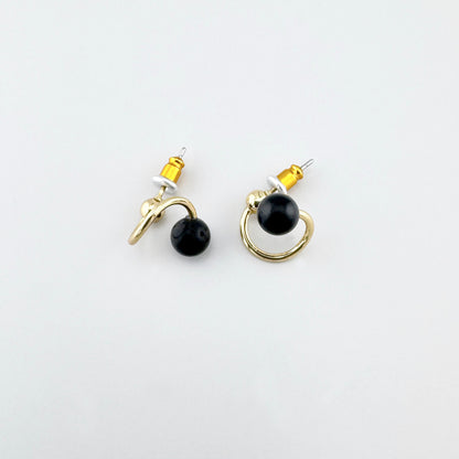Pendientes dorados con piedra negra y silueta en espiral, brillo pulido y cierre de perno para un look limpio