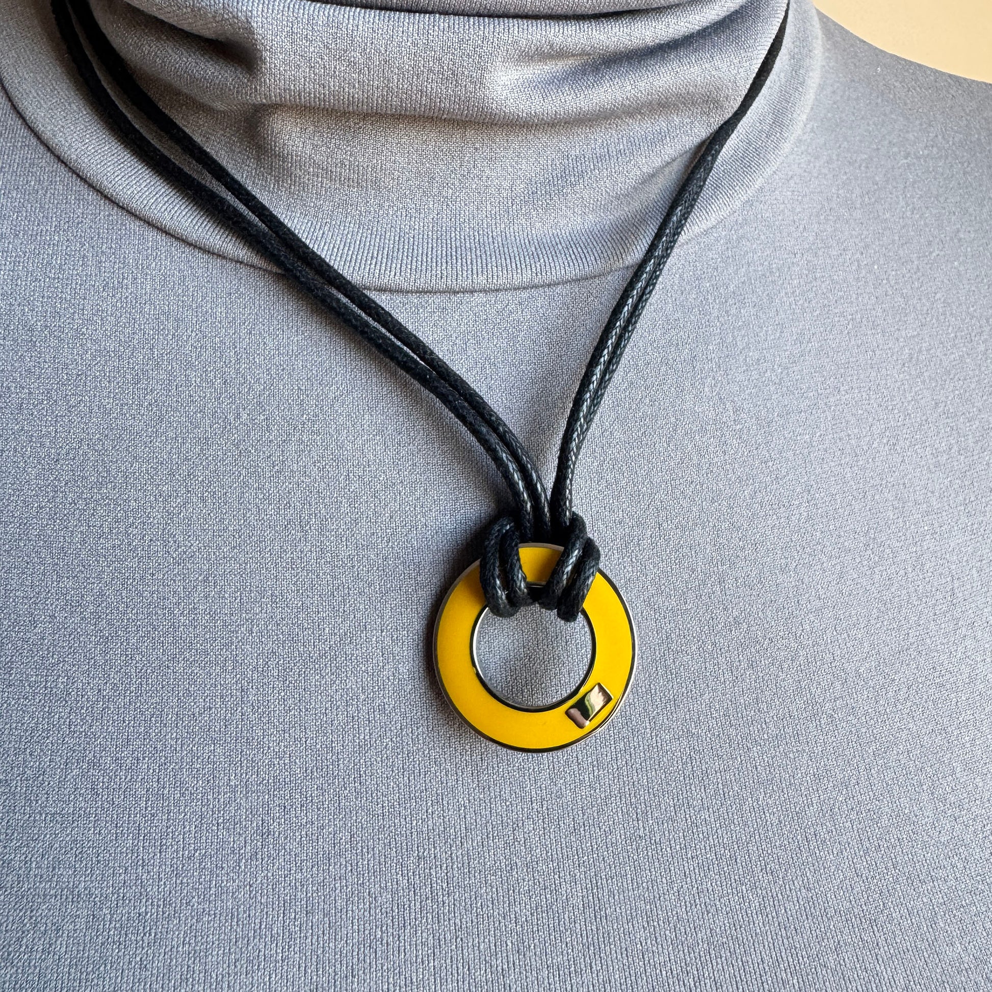 Reversible enamel necklace worn on black cord with yellow pendant