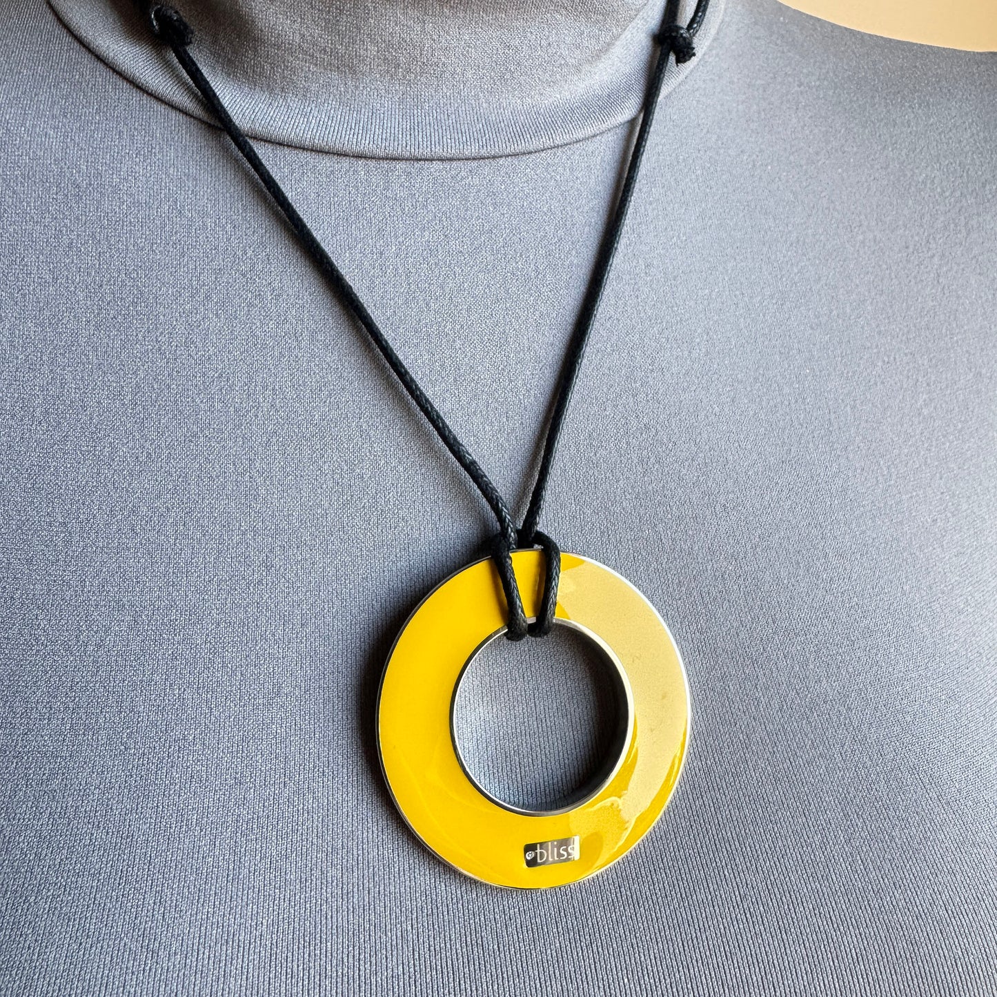 Reversible enamel necklace worn on black cord with yellow pendant