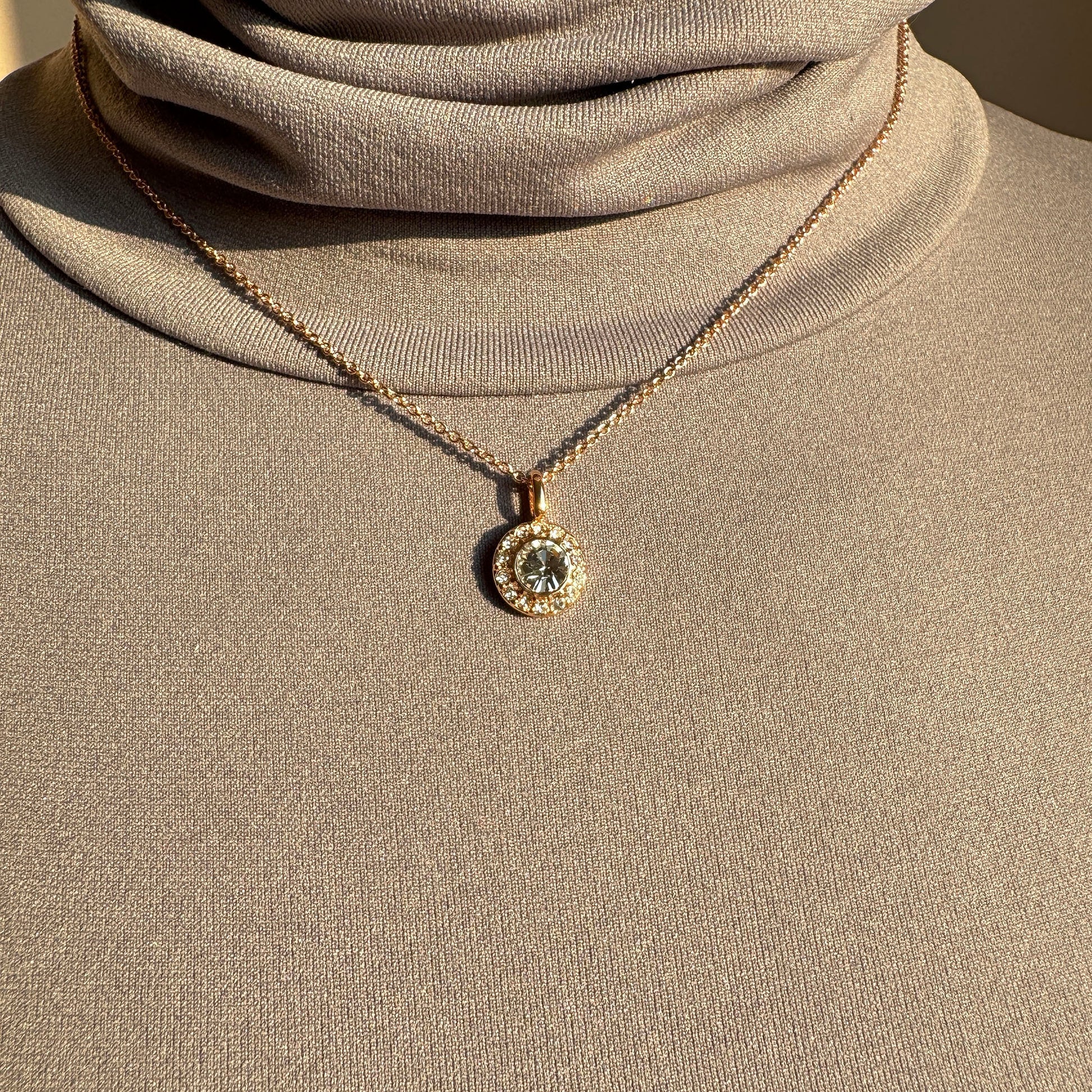Elegant gold-plated necklace with round zirconia pendant styled on a beige top