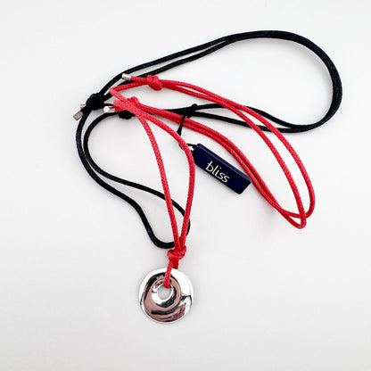 Collar rojo y negro con colgante plateado, detalle minimalista sobre fondo neutro