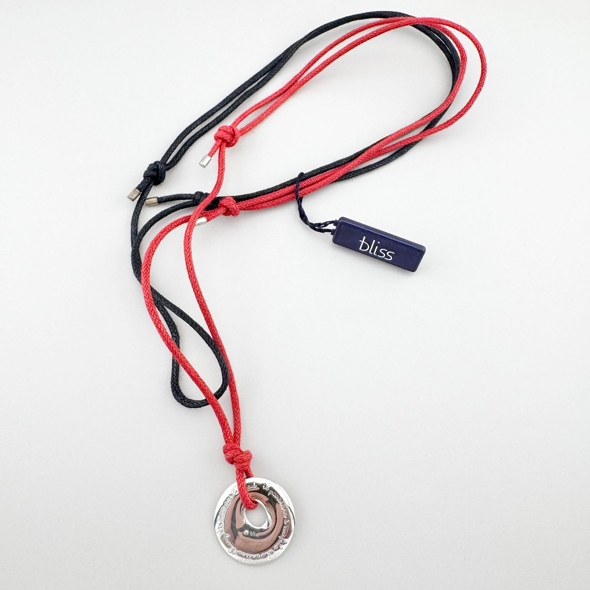 Silberanhänger an rot‑schwarzer Kordel, klare moderne Linie liegend