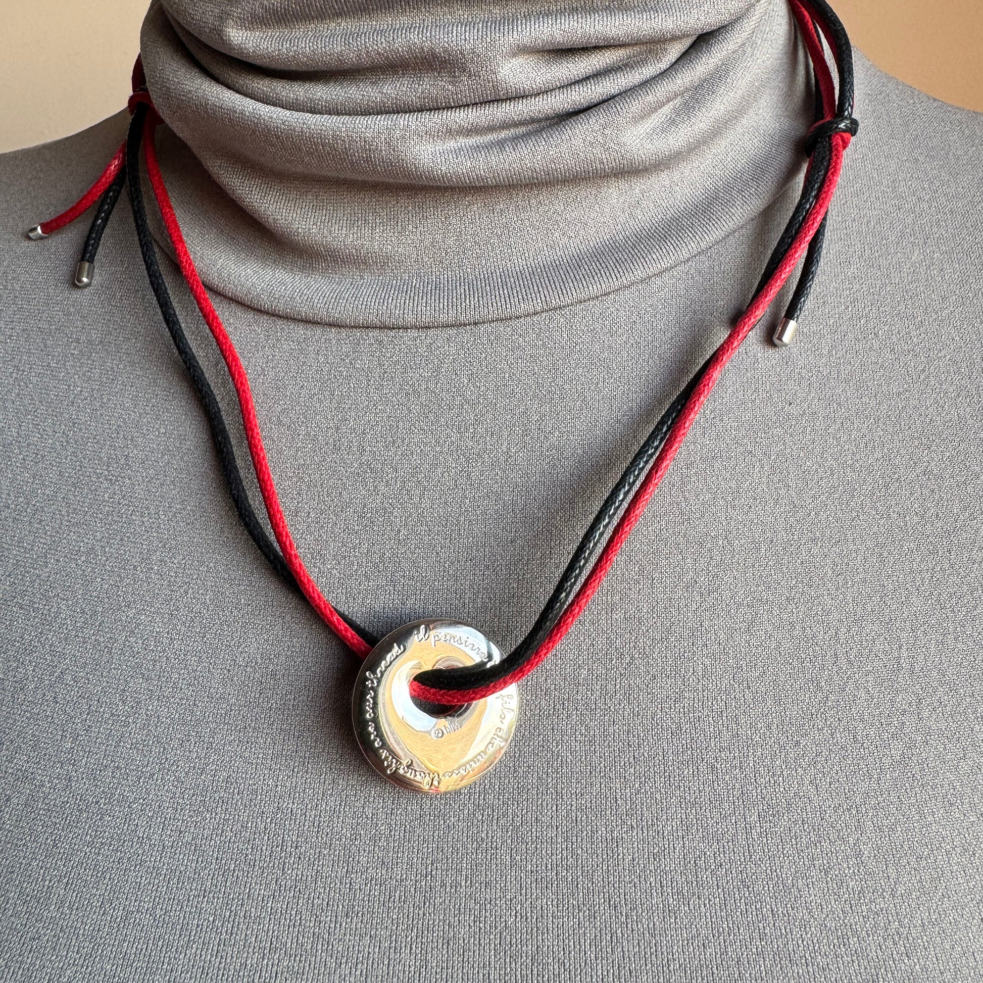 Silver pendant on red and black cord, calm geometric accent near the collarbone
