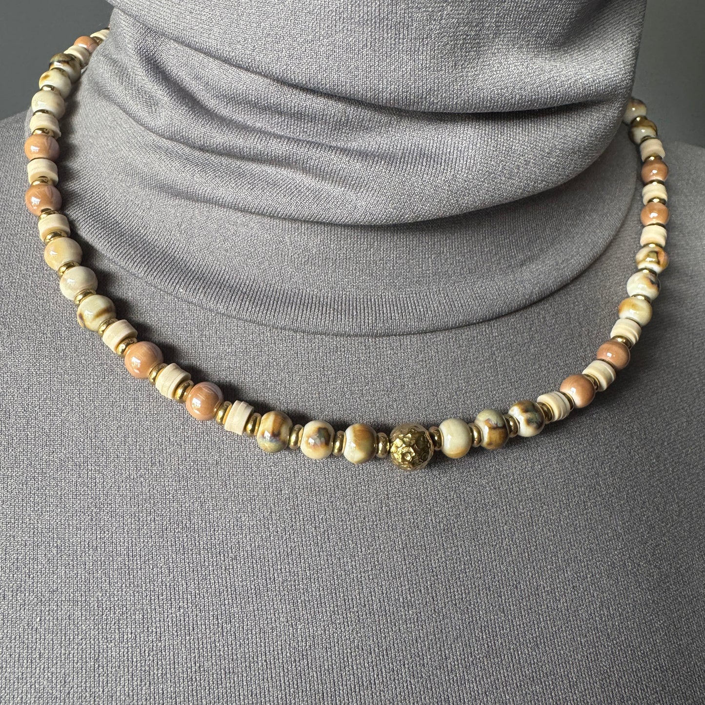 Elegant ceramic bead necklace in golden and beige tones worn around the neck