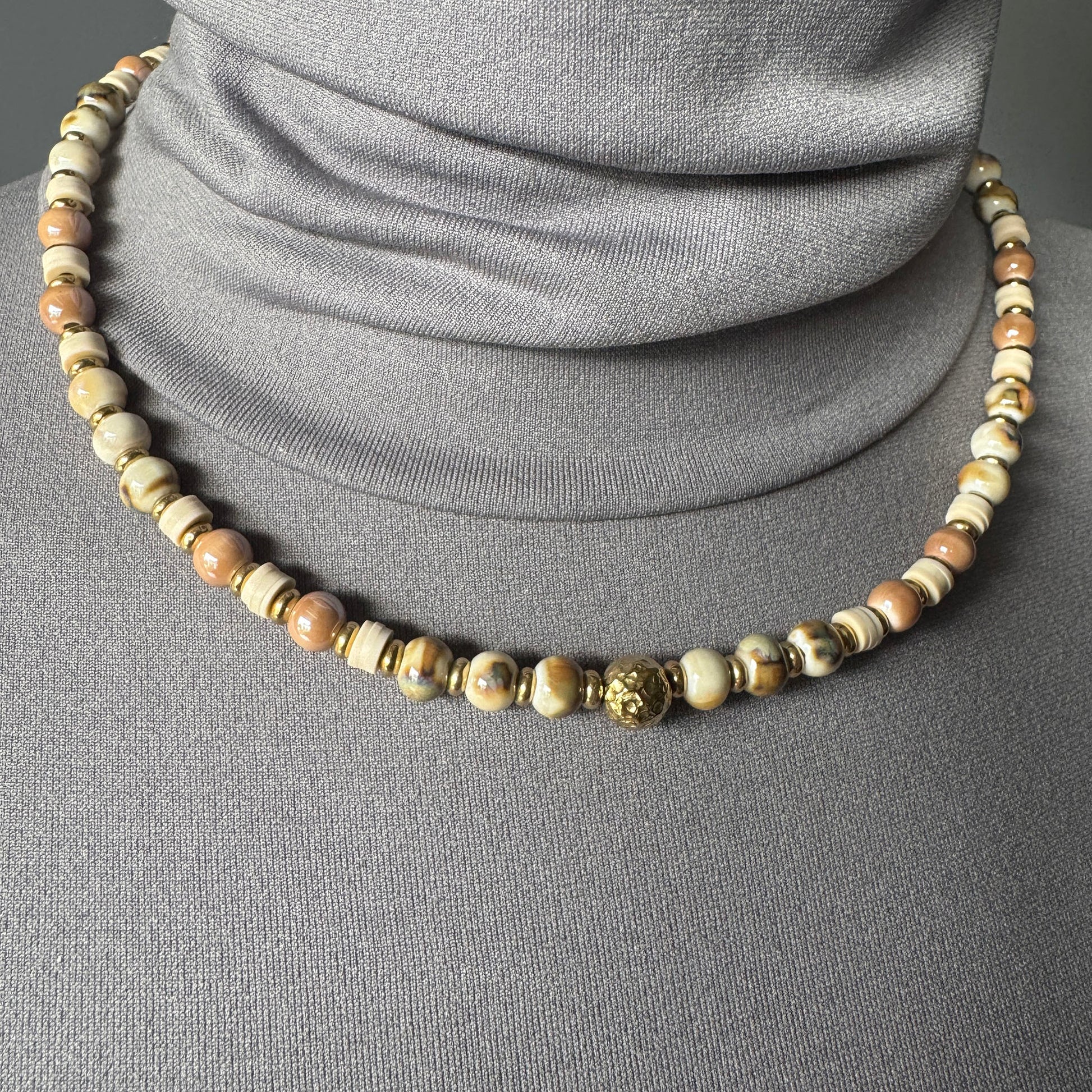 Elegant ceramic bead necklace in golden and beige tones worn around the neck