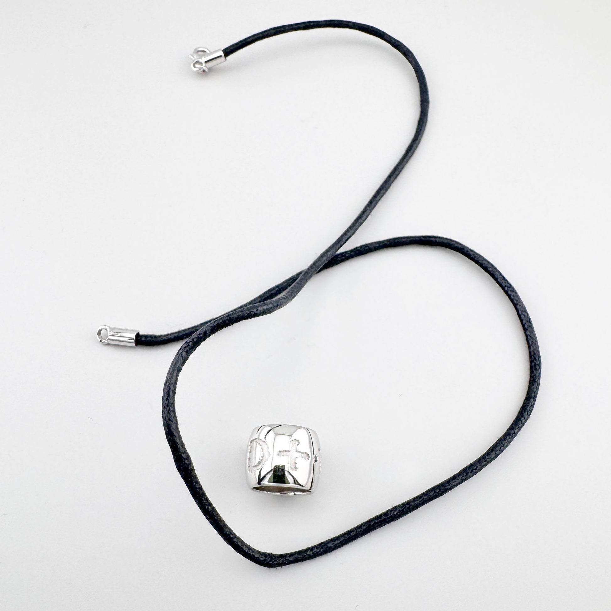 Collar con símbolos grabados sobre cordón negro, expresión sobria y contemporánea